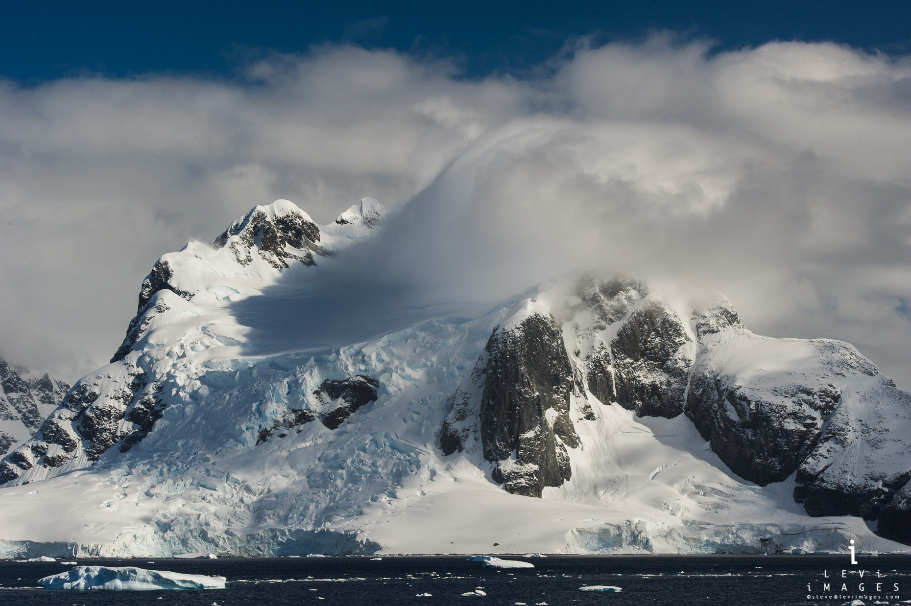 Clouds rush over glacial covered mountains. Lemaire channel, Antarctica