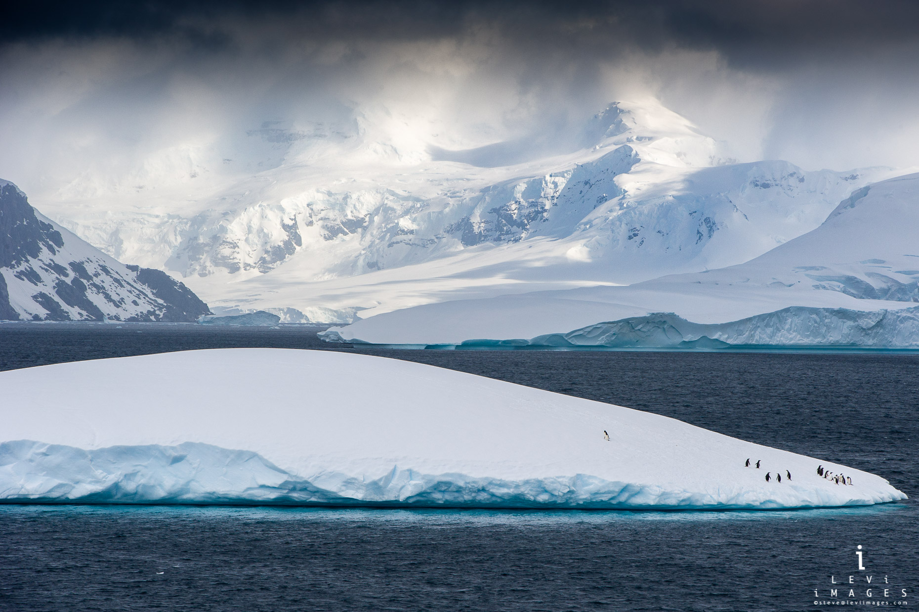 Penguins, mountains and iceberg reflection in low cloud cover, Paulette Island Antarctica